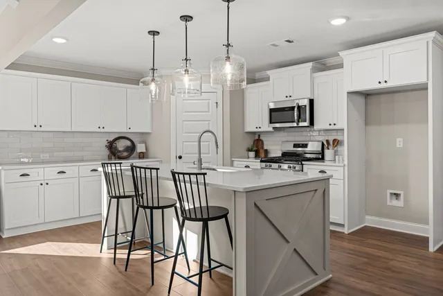 a kitchen with stainless steel appliances kitchen island granite countertop a refrigerator a sink dishwasher a stove and white cabinets with wooden floor