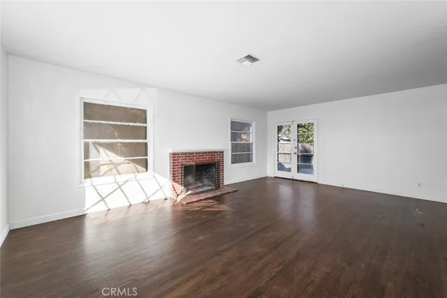 an empty room with wooden floor fireplace and windows