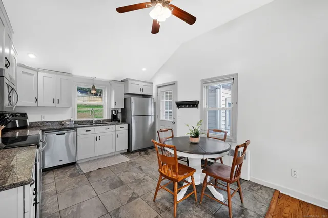 a kitchen with stainless steel appliances kitchen island granite countertop a dining table chairs and a refrigerator