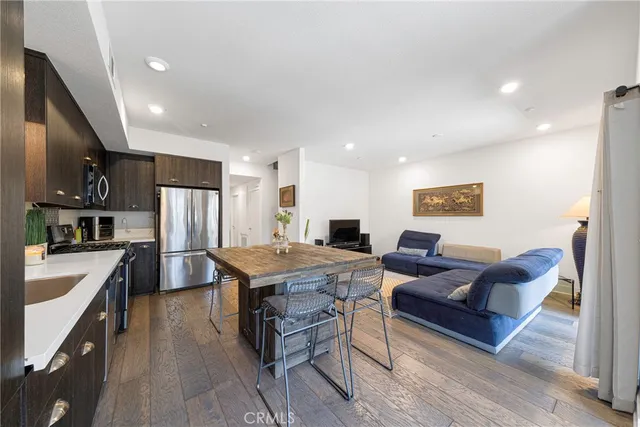 a kitchen with stainless steel appliances granite countertop a refrigerator a stove a sink a dining table and chairs with wooden floor