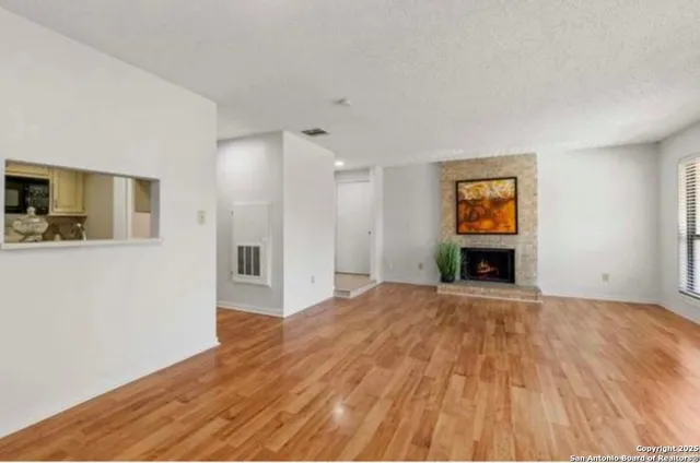 a view of an empty room with wooden floor fireplace and a window