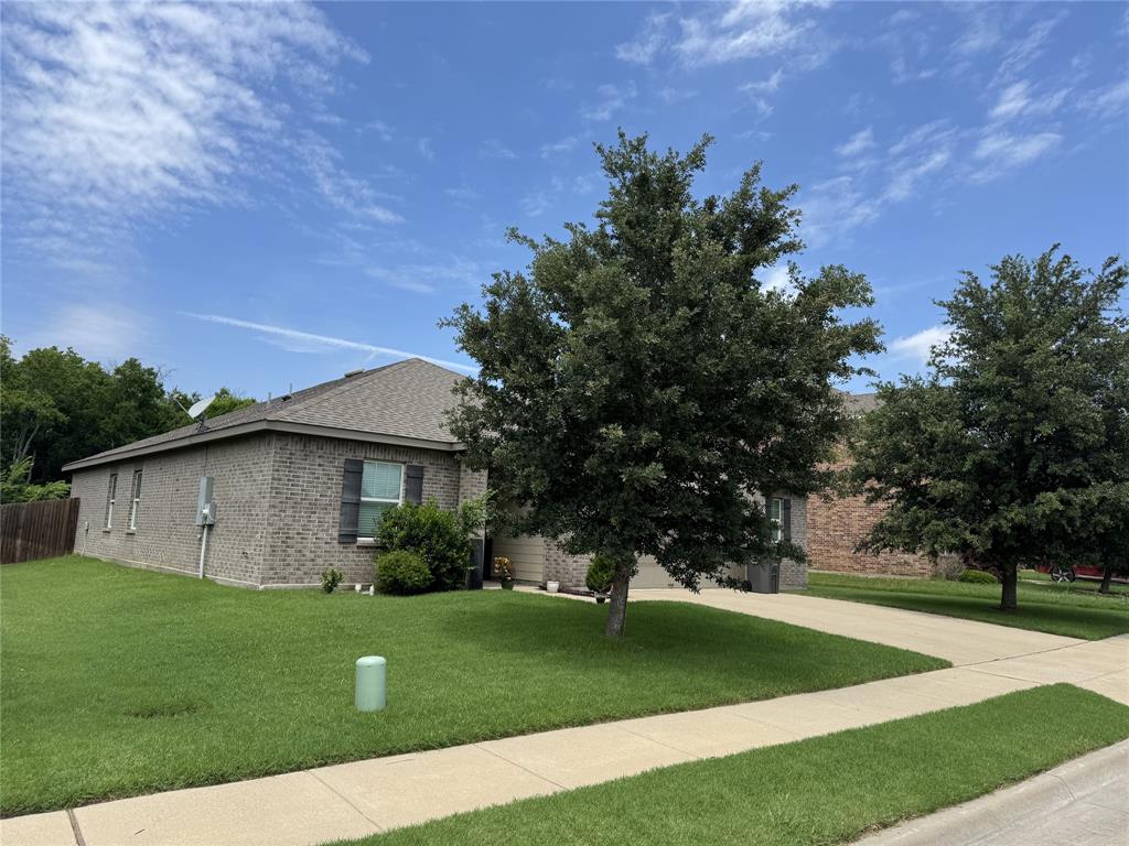 2209 Cinnamon Spgs Road Glenn Heights, TX 75154 - Photo 4 of 28 Gray brick exterior with dark shutters, featuring a manicured lawn and mature trees