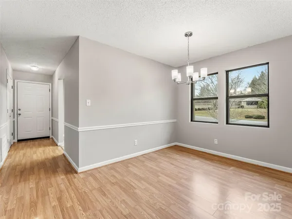 an empty room with wooden floor chandelier and windows