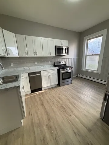 a large kitchen with stainless steel appliances granite countertop a stove top oven a sink dishwasher and white cabinets with wooden floor