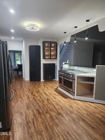 a kitchen with stainless steel appliances granite countertop a refrigerator a sink dishwasher a stove with white cabinets and wooden floor