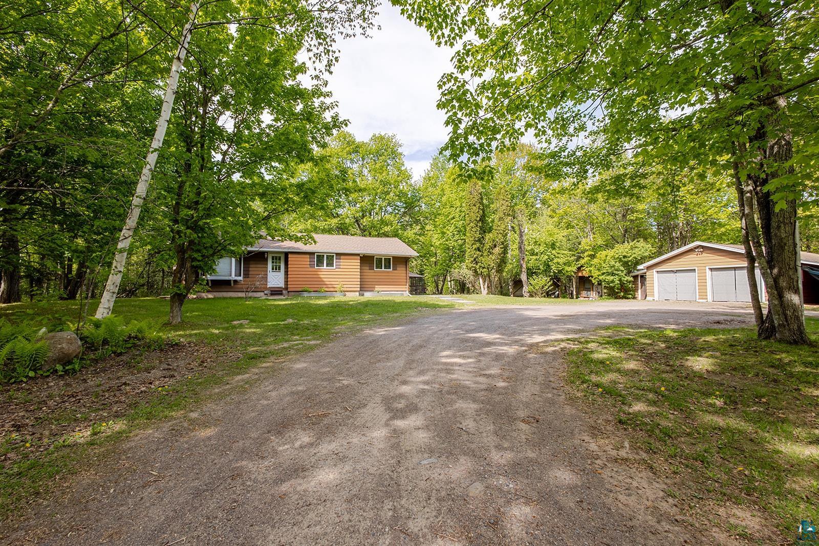 7045 Morris Thomas Road Cloquet, MN 55720 - Photo 1 of 28 Front exterior with brown siding and white trim, featuring a gravel driveway and a detached two-car garage