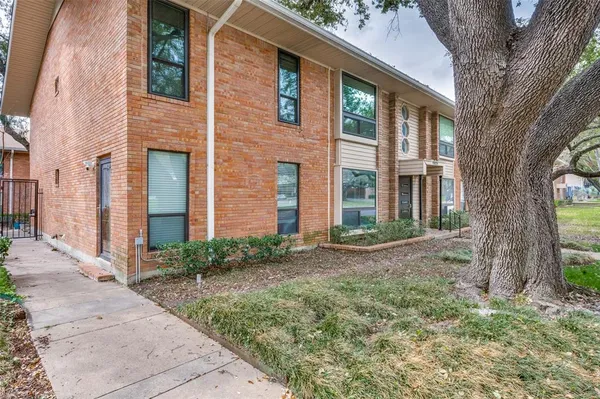 a view of a brick house with many windows plants and large tree