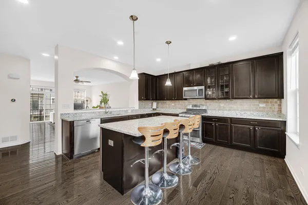 a kitchen with stainless steel appliances granite countertop wooden cabinets a sink dishwasher a stove and a refrigerator with wooden floor