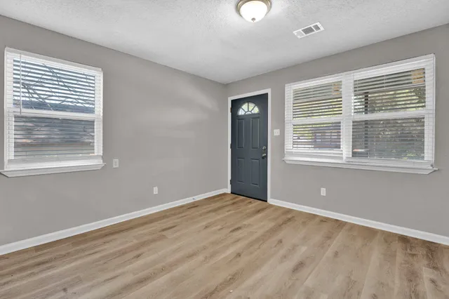 a view of an empty room with wooden floor and a window