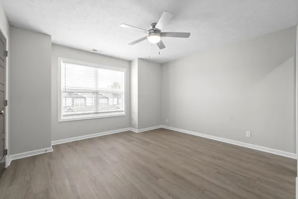 an empty room with wooden floor chandelier fan and windows