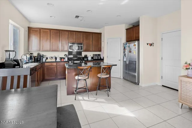 a kitchen with stainless steel appliances kitchen island granite countertop a refrigerator a stove a sink a dining table and chairs with wooden floor