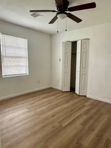 an empty room with wooden floor ceiling fan and windows