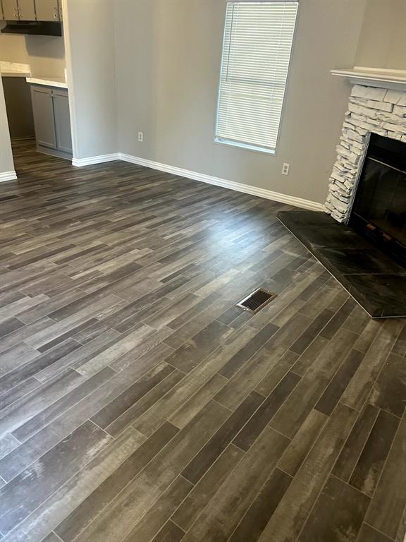 717 Byron Road Wilmer, TX 75172 - Photo 12 of 20 Wood-finish flooring throughout, featuring a stone-clad fireplace with a dark hearth, white baseboards, and a window with blinds