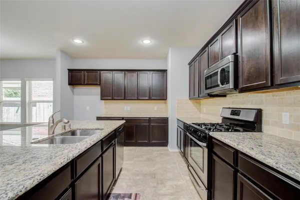 a kitchen with granite countertop stainless steel appliances a sink dishwasher a stove top oven a refrigerator with wooden cabinets and floor