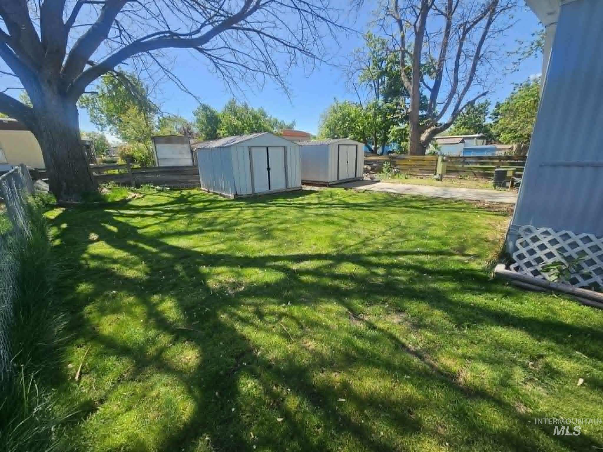 461 Greenleaf Street Boise, ID 83713 - Photo 18 of 19 Expansive grassy yard featuring a substantial mature tree, two detached metal storage sheds, and a partial chain-link fence