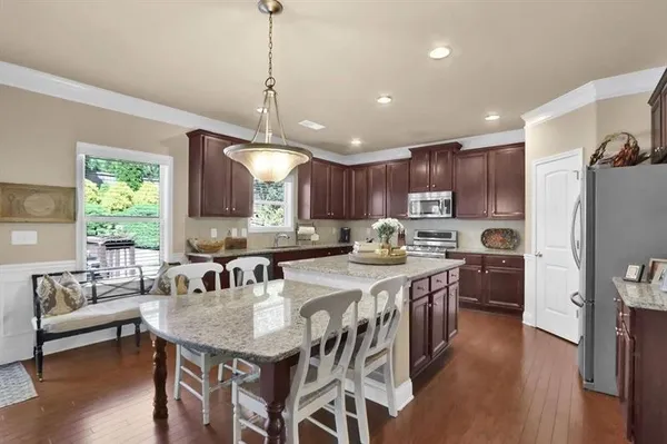 a kitchen with stainless steel appliances granite countertop a stove a refrigerator a kitchen island a sink dishwasher a dining table and chairs with wooden floor