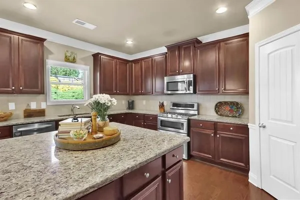 a kitchen with kitchen island granite countertop wooden cabinets a stove a sink and dishwasher with wooden floor