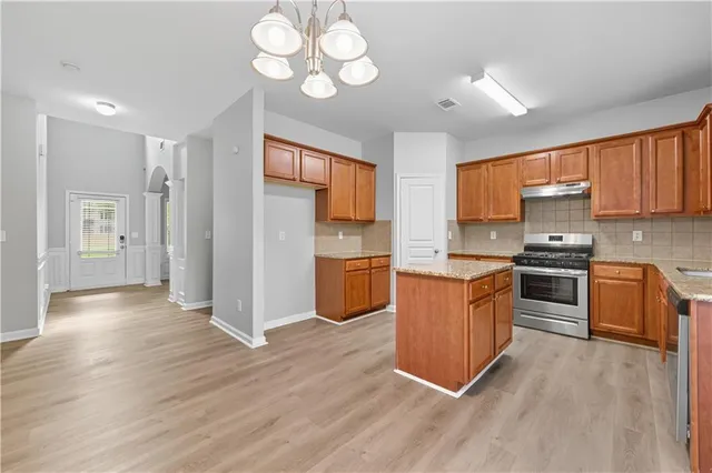 a kitchen with stainless steel appliances granite countertop a refrigerator a stove top oven a sink dishwasher and wooden cabinets with wooden floor