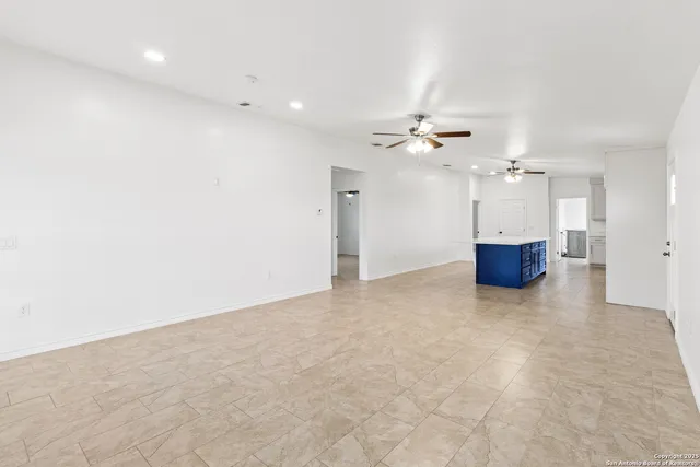 an empty room with a ceiling fan and kitchen view