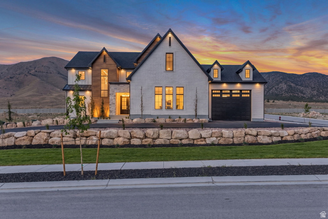 2828 Jojo Road Eagle Mountain, UT 84005 - Photo 1 of 63 Modern farmhouse exterior featuring an attached two-car garage, stone retaining walls, a paved driveway, and established landscaping