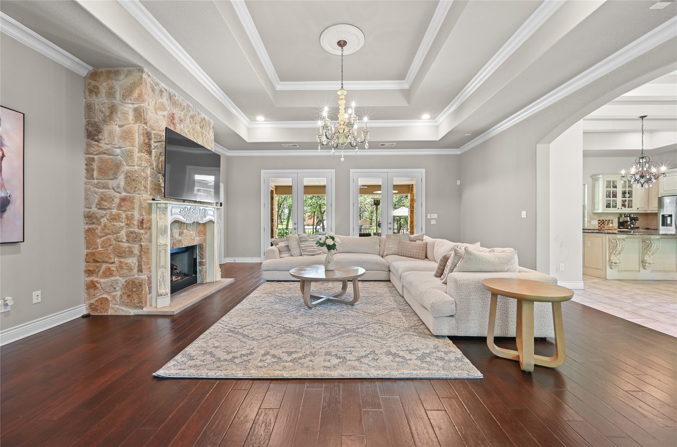387 Corral Road Smithville, TX 78957 - Photo 4 of 40 Living area featuring a stone accent wall fireplace with an ornate mantel, dark wood-finish flooring, and a coffered ceiling with a chandelier