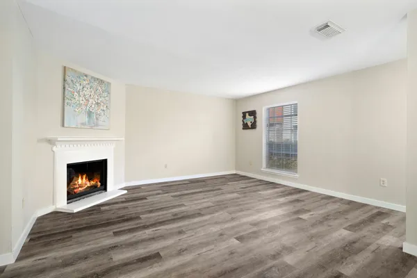 a view of an empty room with wooden floor fireplace and a window