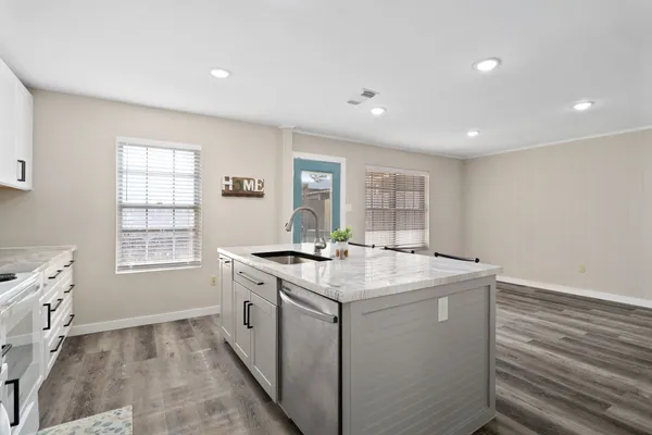 a kitchen with sink stove and white cabinets with wooden floor
