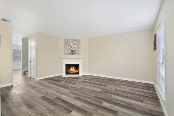 a view of an empty room with wooden floor fireplace and a window