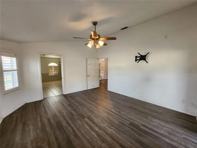 a view of an empty room with wooden floor and a ceiling fan