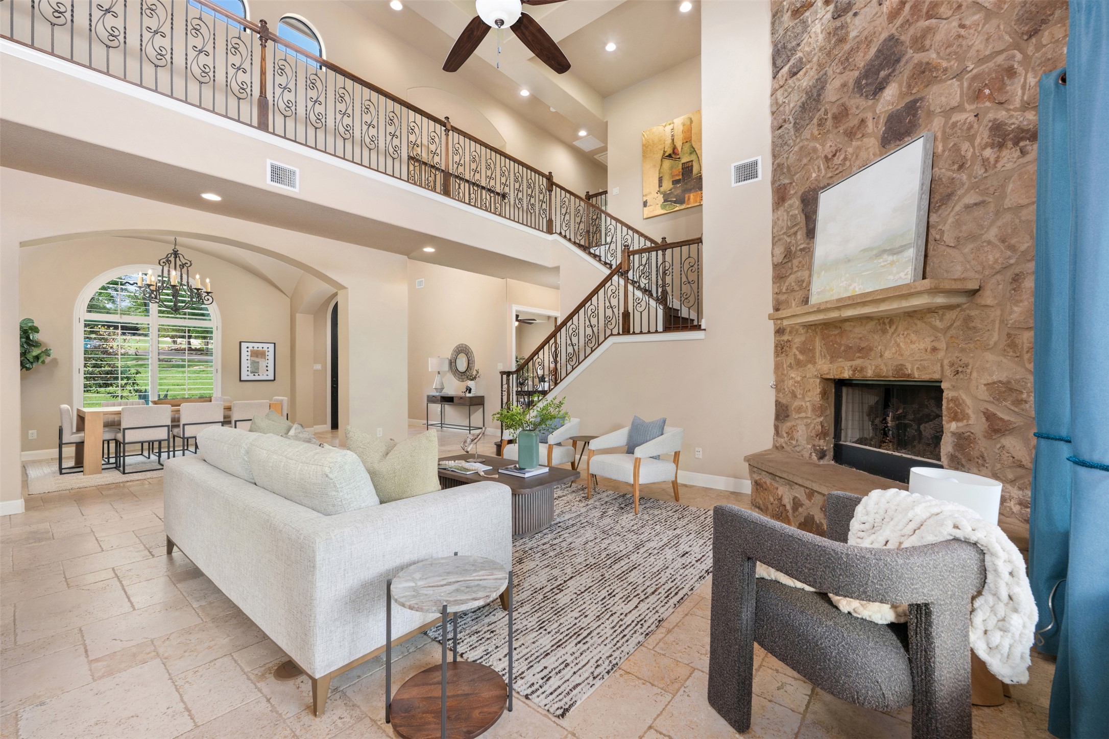 1102 Paw Print Leander, TX 78641 - Photo 11 of 40 The living area features high ceilings, a stone fireplace, and an ornate staircase with wrought iron railings, complemented by large tile flooring