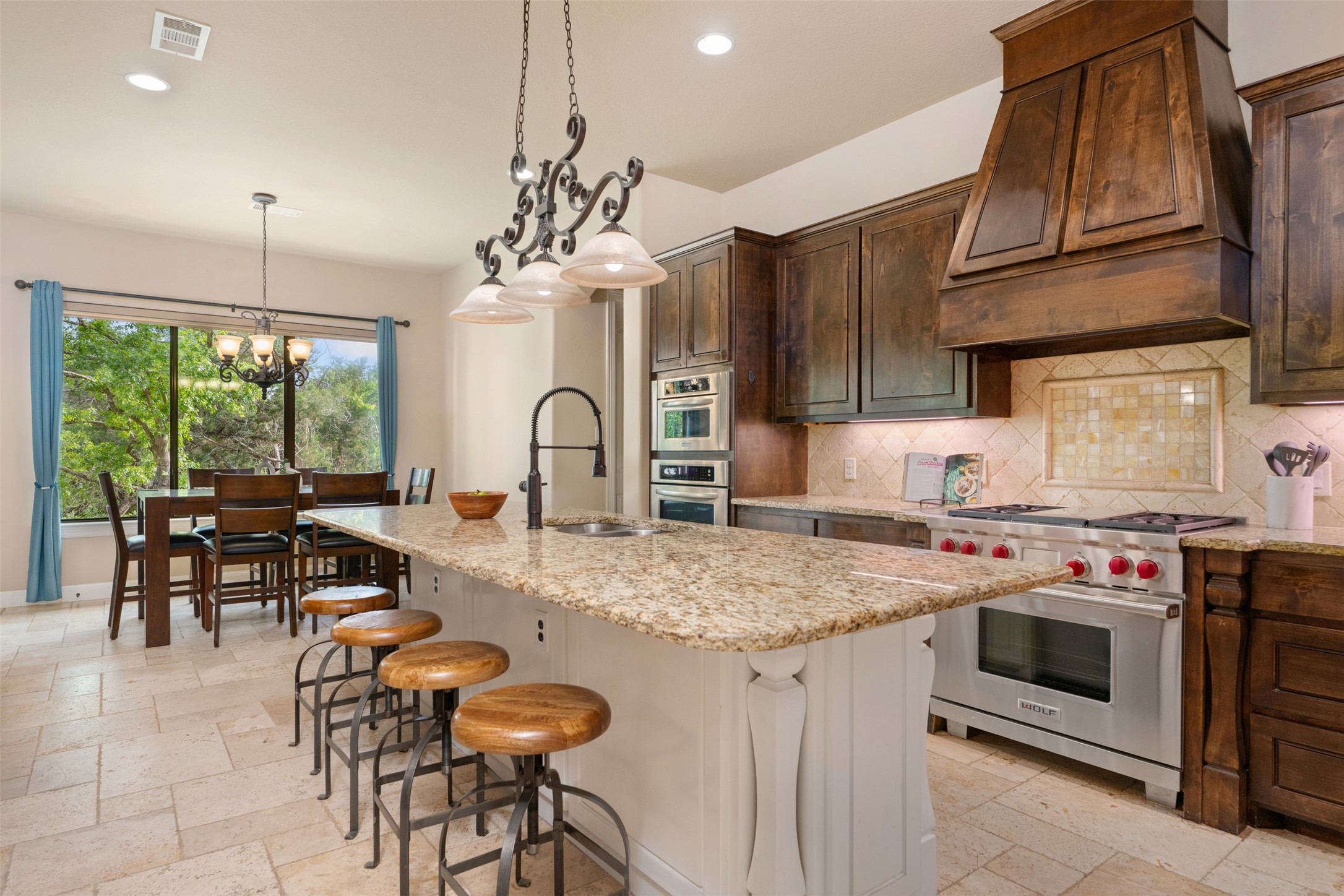 1102 Paw Print Leander, TX 78641 - Photo 13 of 40 A spacious kitchen featuring a large island with a granite countertop, a gas range with a custom wood hood, and rich wood cabinetry