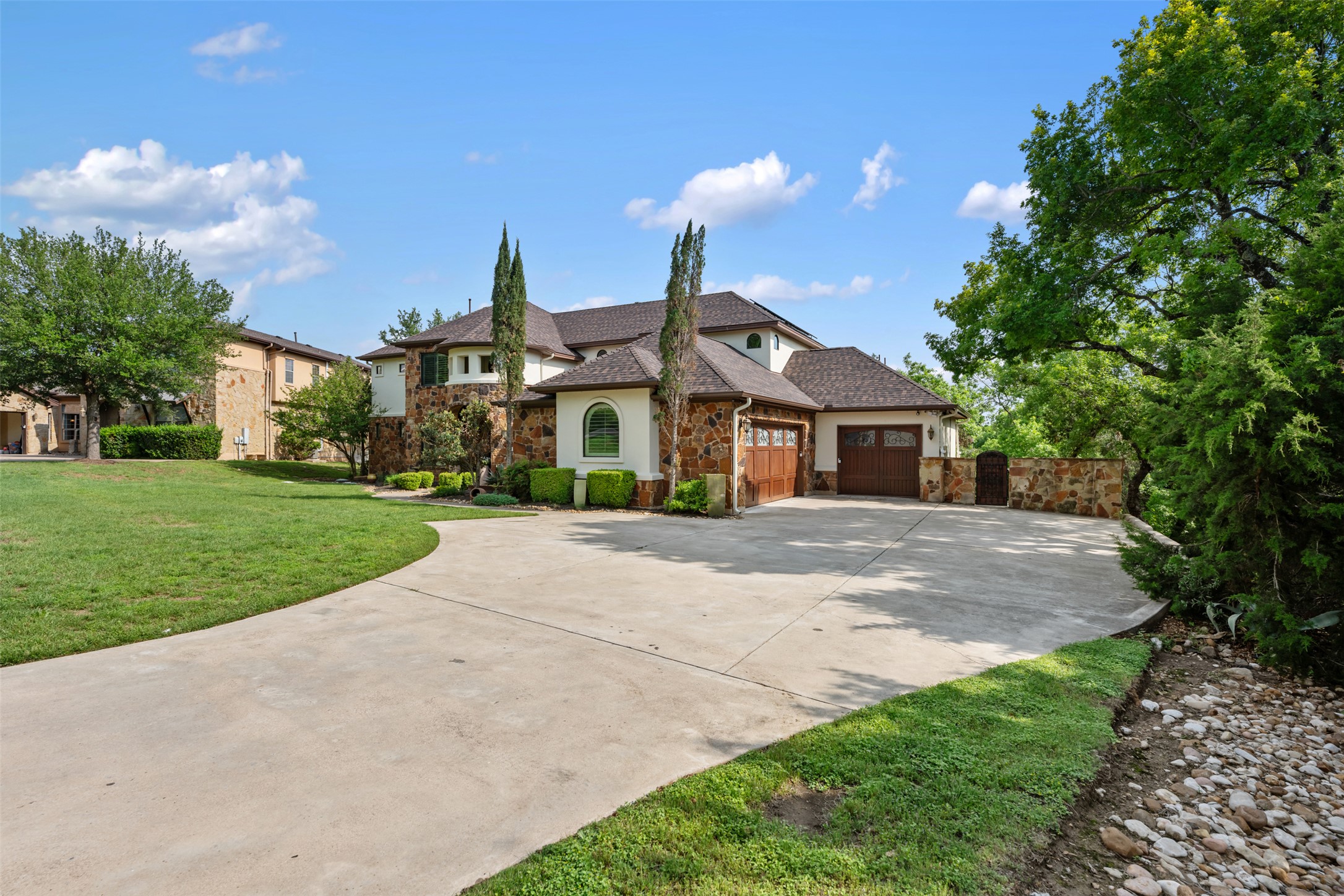 1102 Paw Print Leander, TX 78641 - Photo 3 of 40 The property features an extensive concrete driveway, a stone and stucco exterior, and a two-car garage with wood-paneled doors