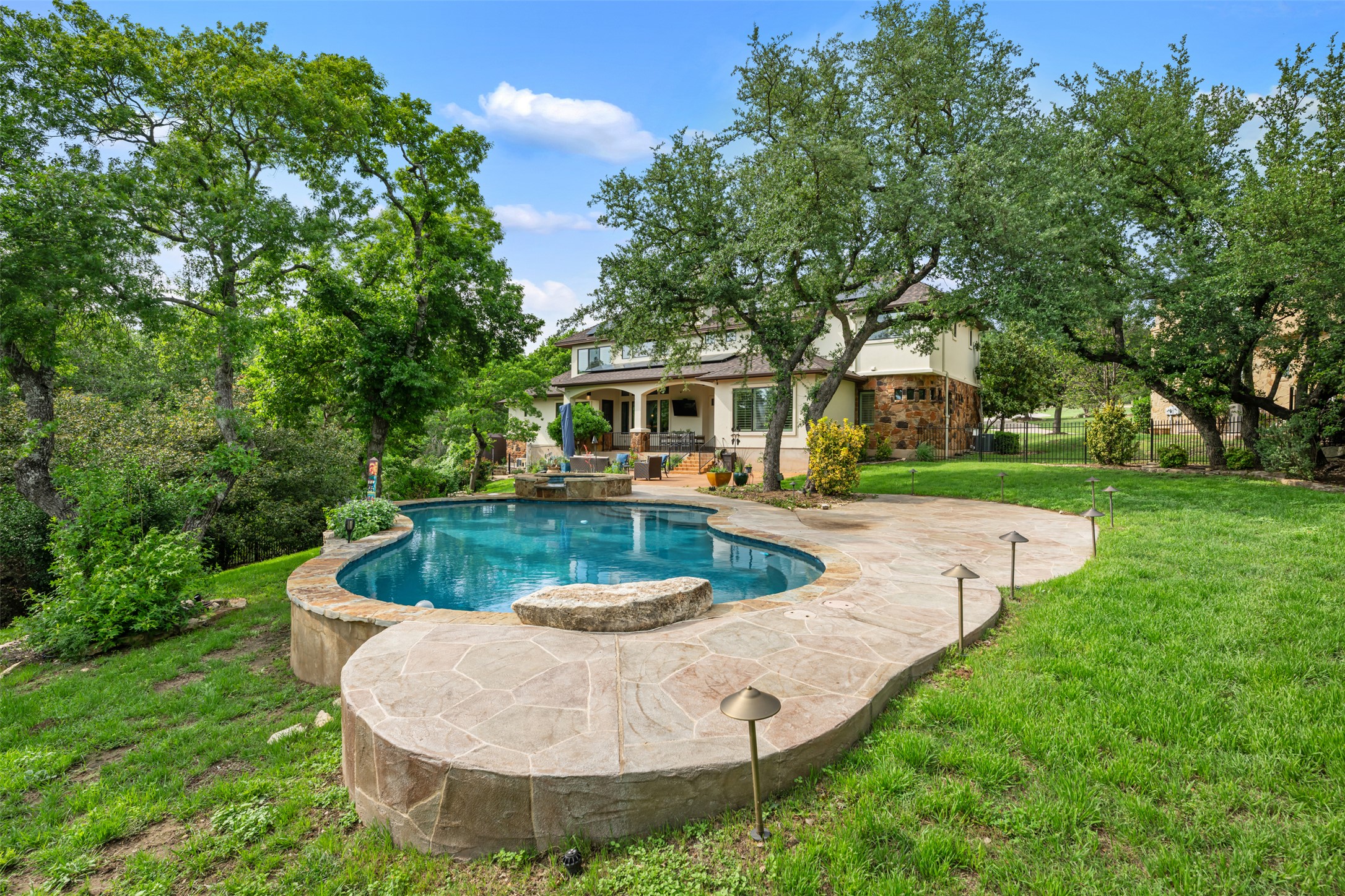 1102 Paw Print Leander, TX 78641 - Photo 31 of 40 The property features a beautifully shaped pool with stone coping, a spacious stone patio, and a well-maintained lawn, all surrounded by mature trees