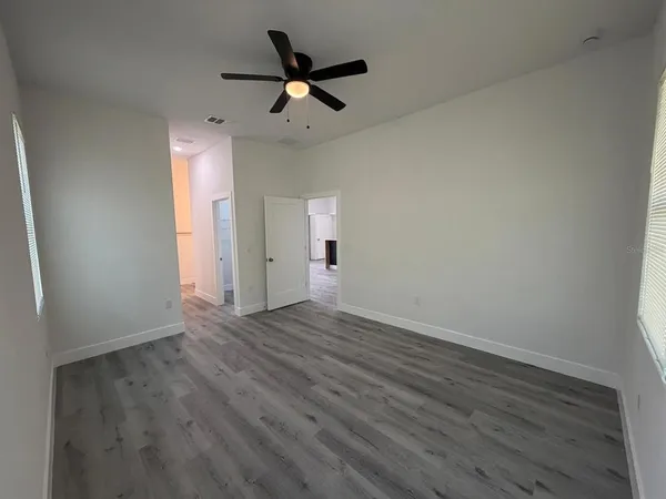 an empty room with wooden floor fan and windows