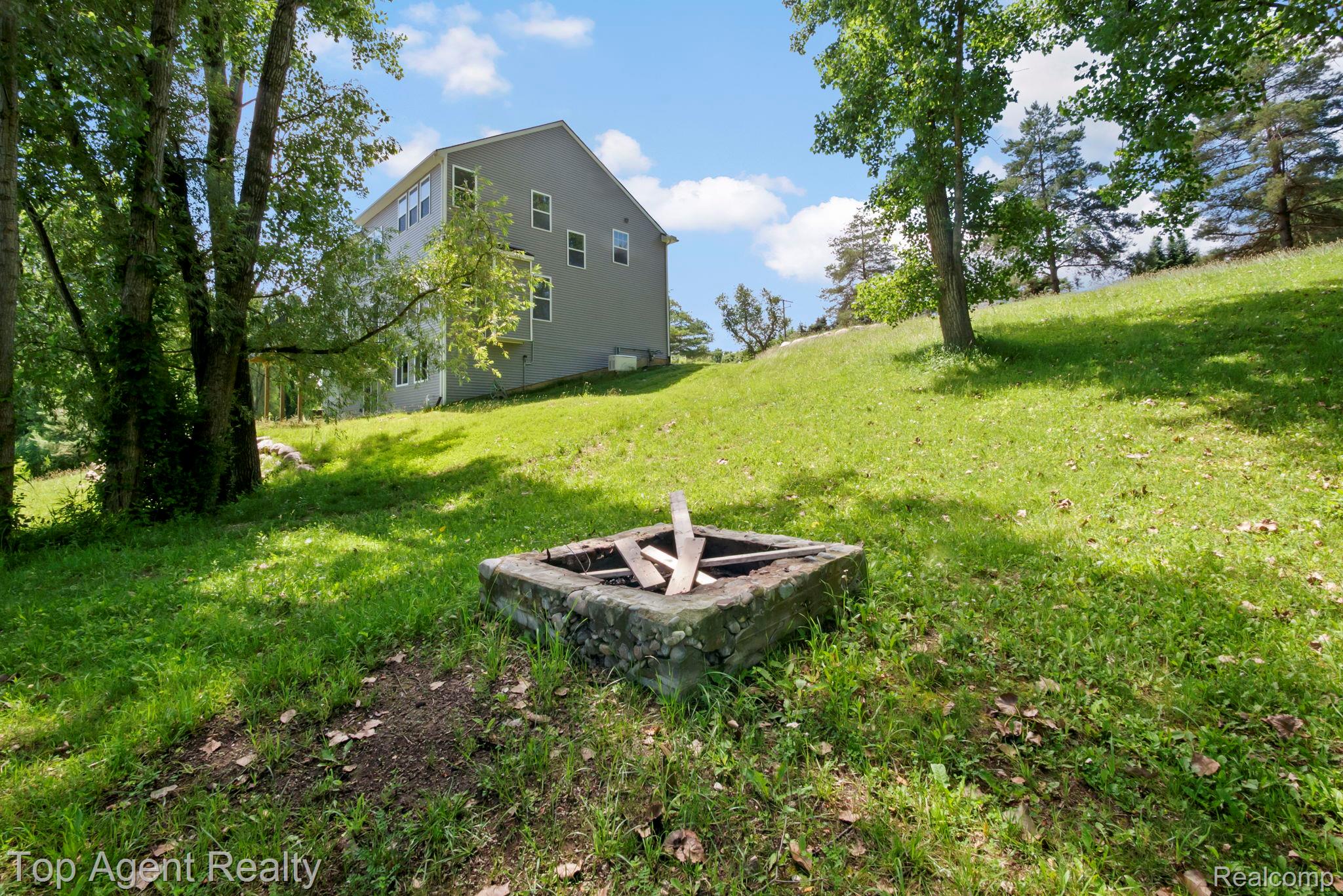 63770 Dequindre Road Washington, MI 48095 - Photo 60 of 61 Expansive grassy yard featuring a built-in fire pit, mature trees, and a multi-story residence with light gray siding and multiple windows