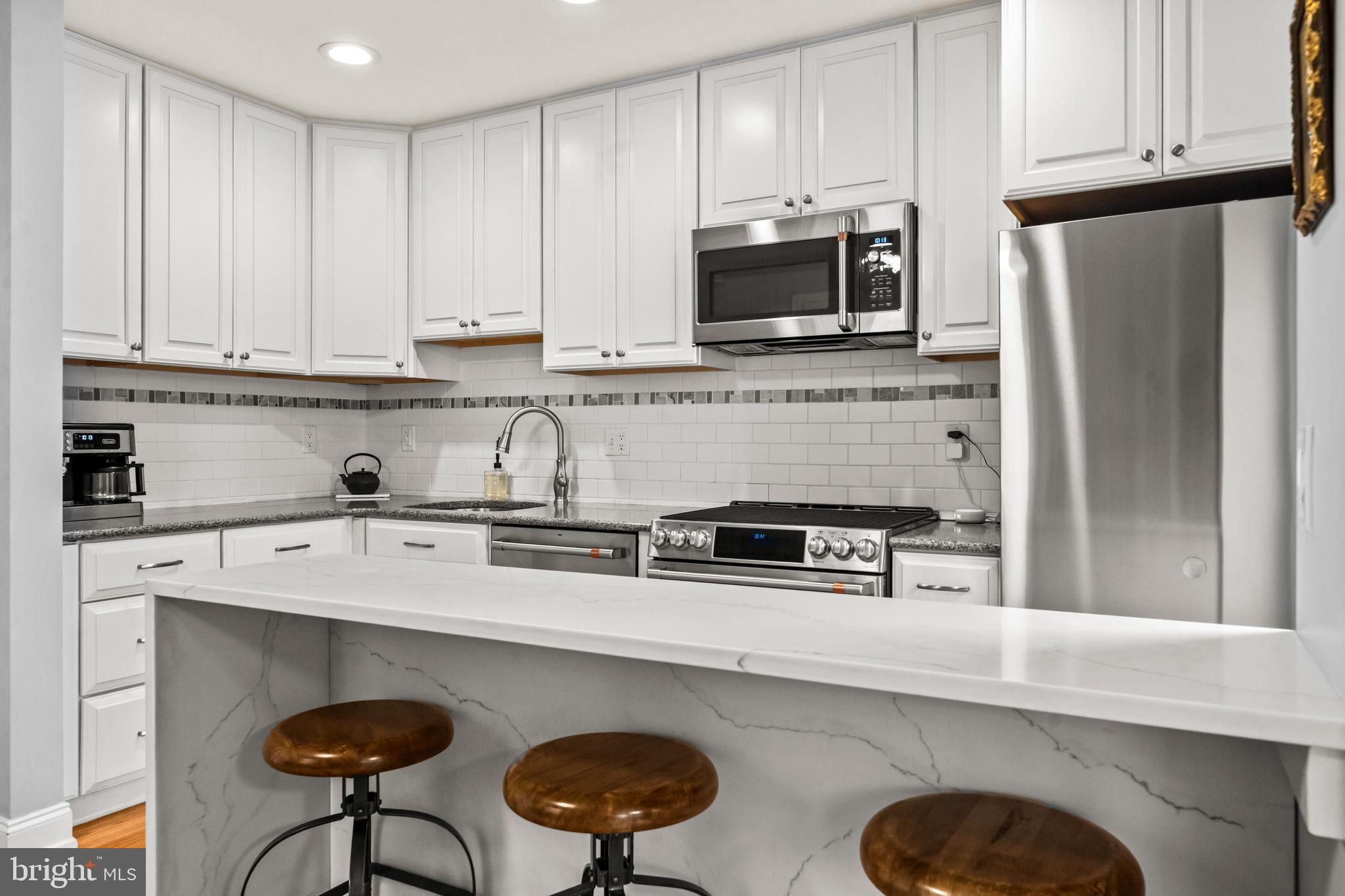 4228 40th Street Northwest Washington, DC 20016 - Photo 12 of 57 a kitchen with stainless steel appliances granite countertop a sink a stove a microwave a refrigerator and white cabinets
