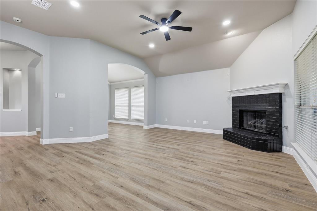 2616 Hollow Ridge Drive Denton, TX 76210 - Photo 11 of 31 Spacious living area featuring wood-finish flooring, a vaulted ceiling, and a prominent fireplace with a black brick surround and white mantel