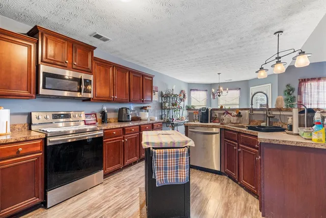 a kitchen with stainless steel appliances granite countertop a stove top oven a sink dishwasher a dining table and chairs with wooden cabinets