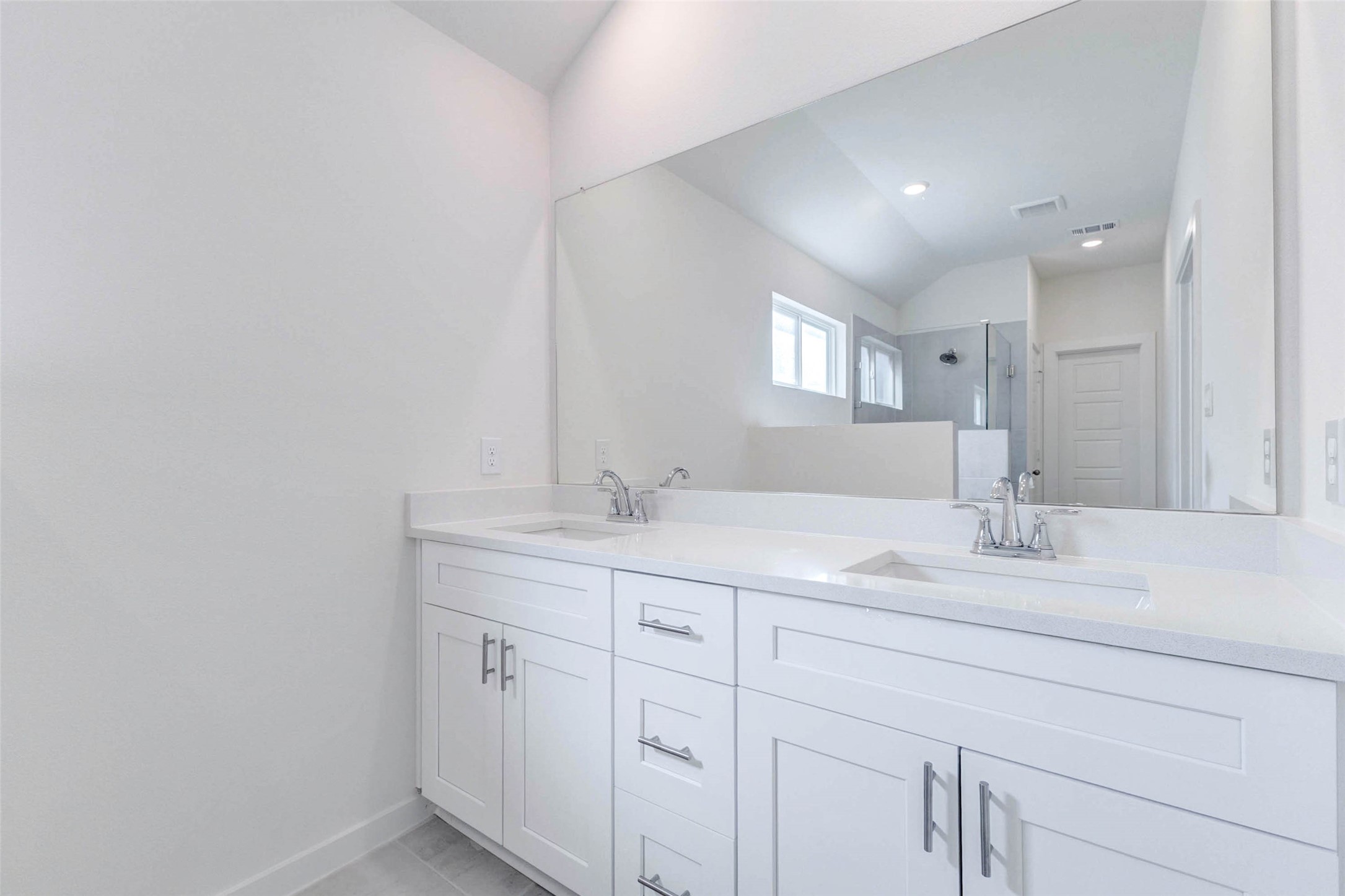 6467 Escondido Drive Rosharon, TX 77583 - Photo 18 of 32 Bright primary bathroom vanity with dual undermount sinks, white shaker cabinetry, chrome fixtures, sleek hardware, and a large wall mirror. The clean neutral palette, light countertops, and spacious cabinet storage create a polished, functional space with a fresh new-construction feel.