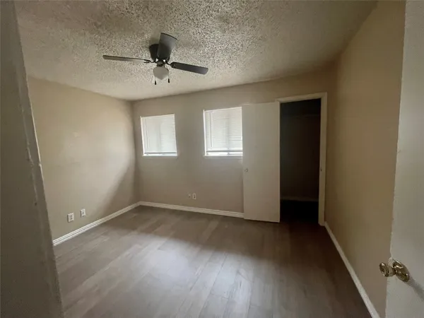 an empty room with wooden floor chandelier fan and windows