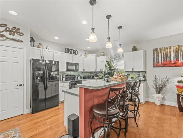 a kitchen with stainless steel appliances kitchen island granite countertop a dining table chairs sink and cabinets