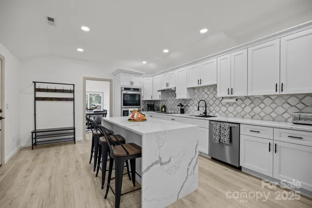 a kitchen with stainless steel appliances kitchen island granite countertop a table chairs sink and cabinets