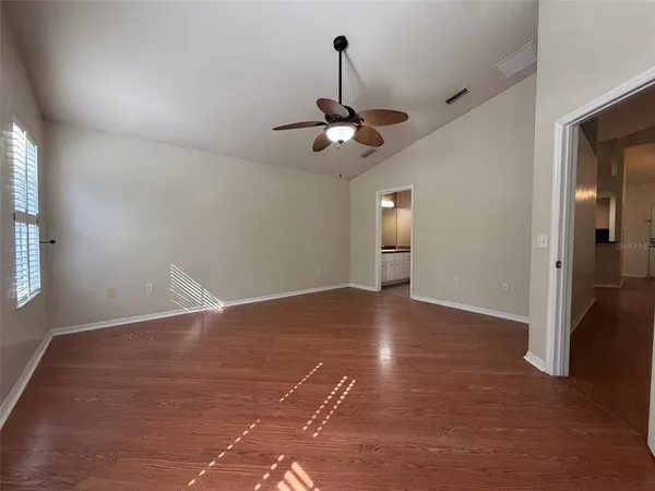 a view of an empty room and chandelier fan and kitchen view