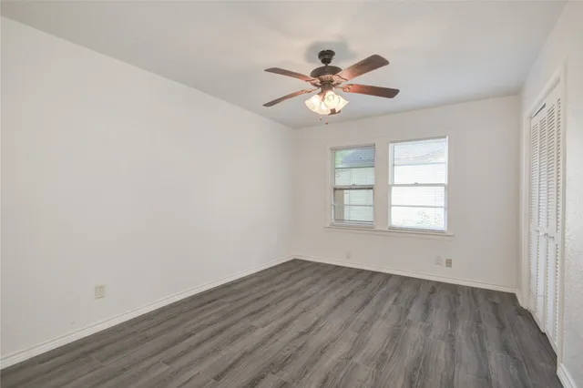 an empty room with wooden floor fan and windows