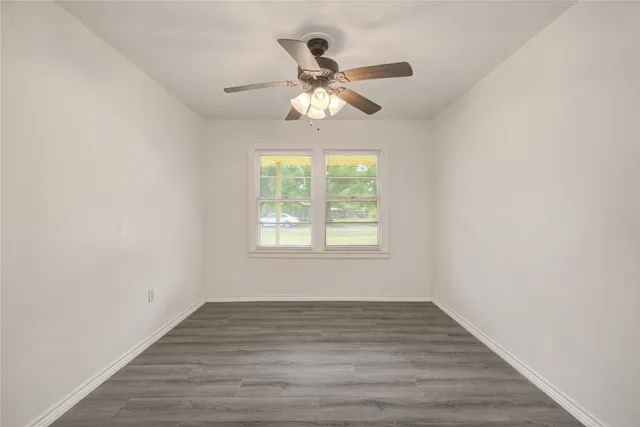 an empty room with wooden floor fan and windows