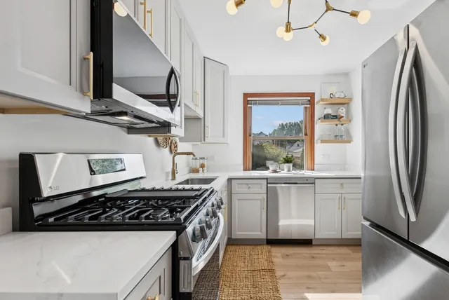 a kitchen with stainless steel appliances a refrigerator a sink a stove and white cabinets