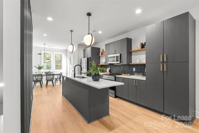 a kitchen with stainless steel appliances granite countertop a refrigerator a sink dishwasher a stove and a dining table with wooden floor