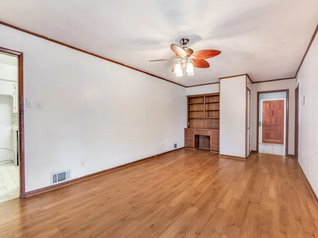 an empty room with wooden floor chandelier fan and windows