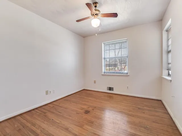 an empty room with wooden floor ceiling fan and windows