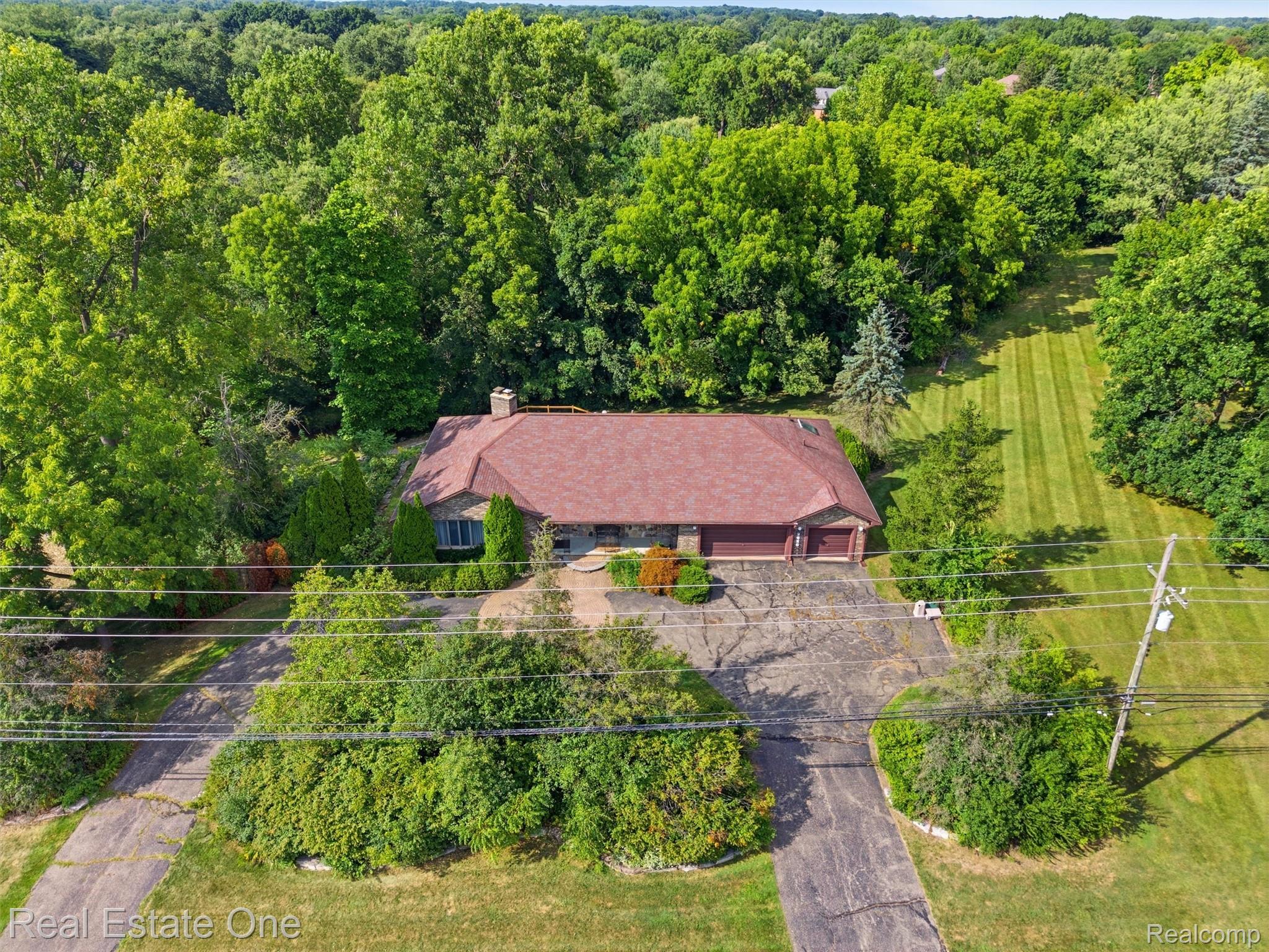 2626 West Wattles Road Troy, MI 48098 - Photo 56 of 65 Stone exterior featuring a red shingle roof, attached two-car garage, and a lush, tree-lined property
